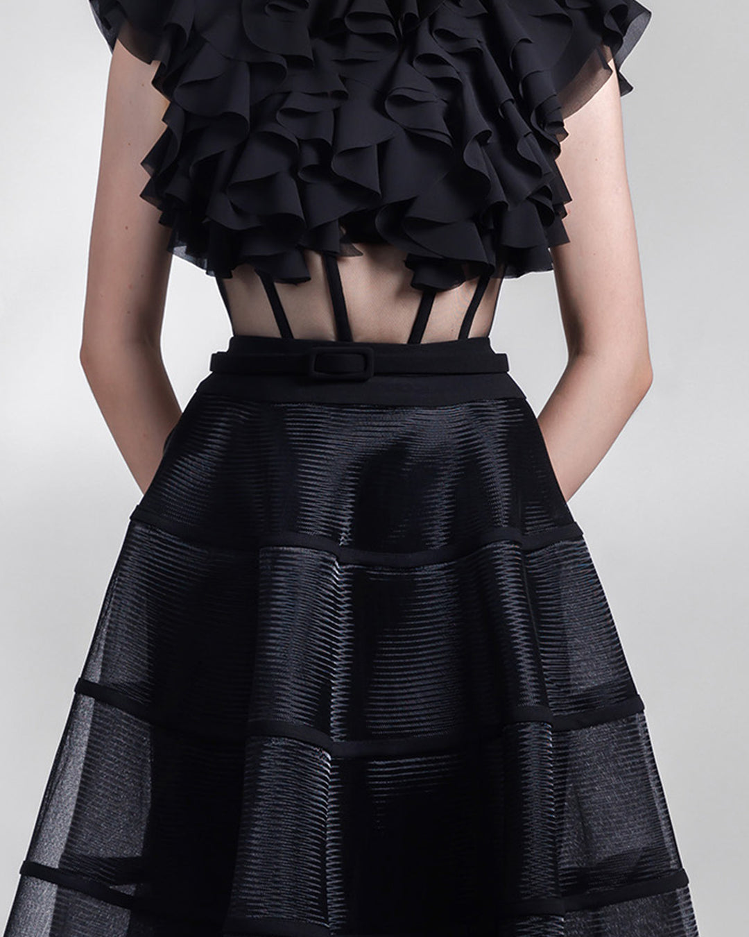 A close-up of an evening wear set featuring a ruffled laser cut open back chiffon top with a see-through corseted bodice paired with a cage like long skirt.