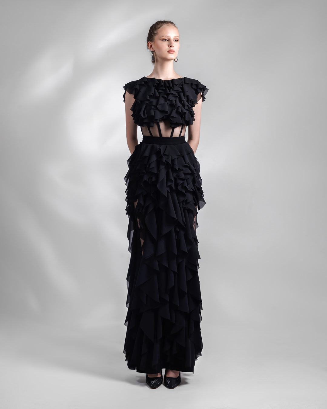 A long fully ruffled chiffon black evening dress featuring a see-through corseted bodice and cutouts on the sides of the skirt.