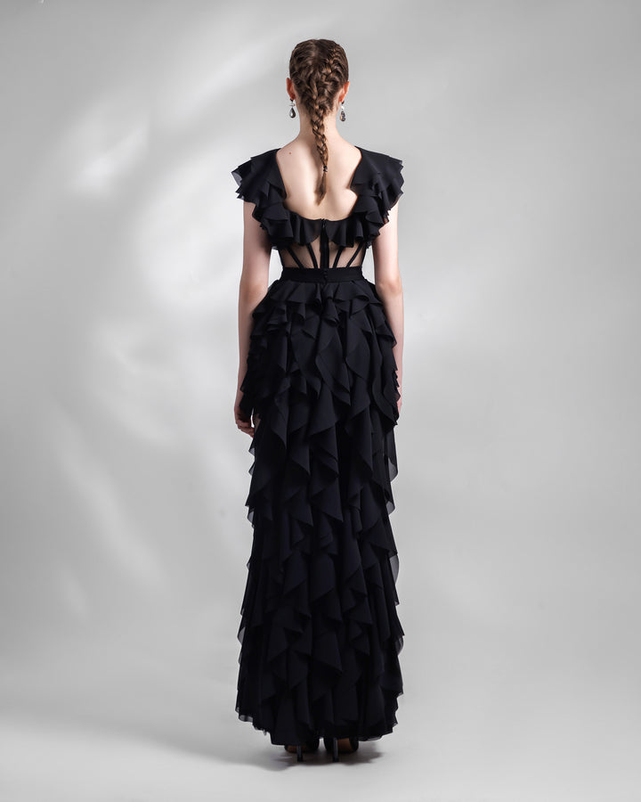 The back of a long fully ruffled chiffon black evening dress featuring a slightly open back and a see-through corseted bodice.