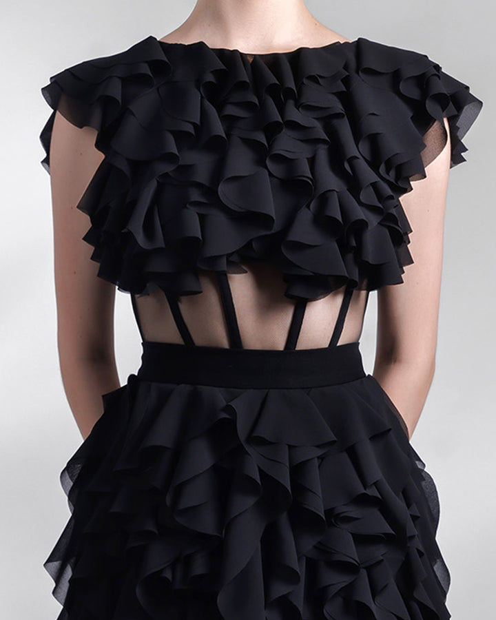 A close-up of a long fully ruffled chiffon black evening dress featuring a see-through corseted bodice.