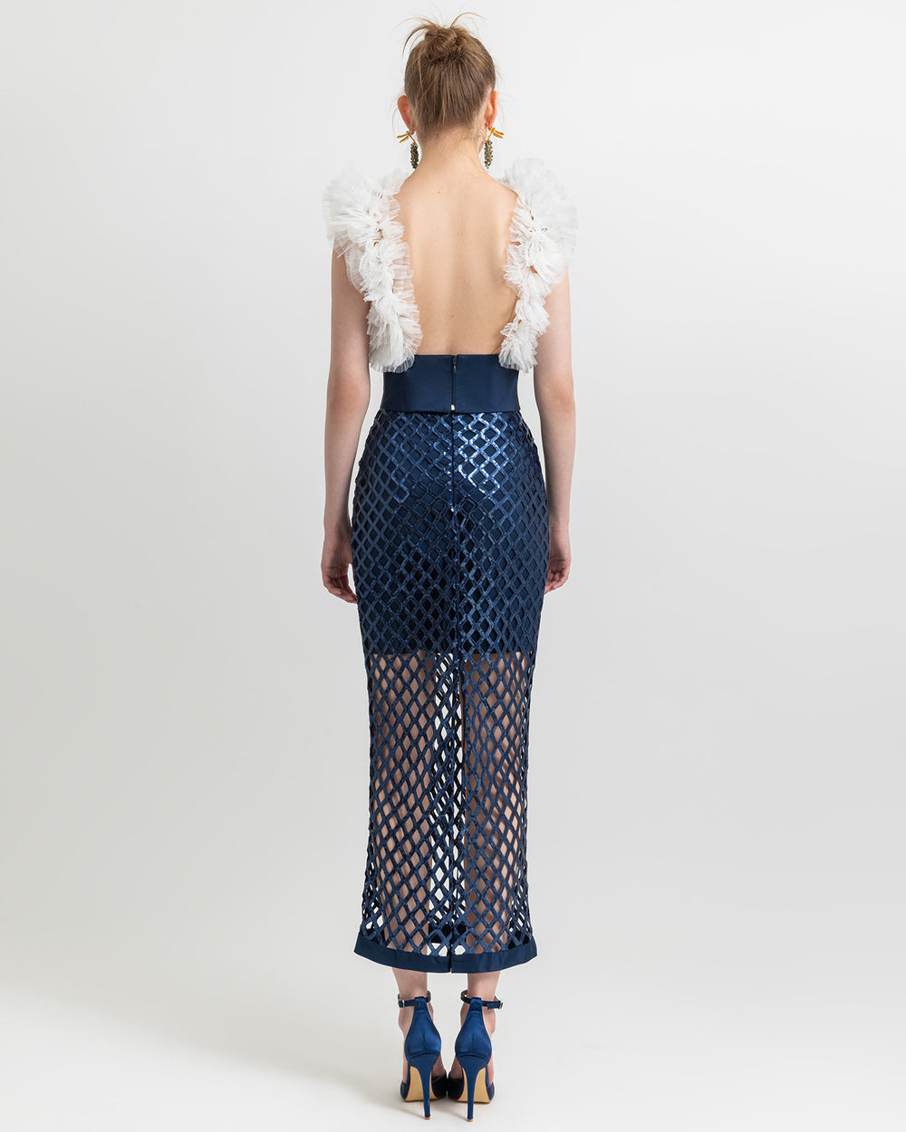 The back of an occasion outfit featuring a backless white tulle top paired with see-through midi navy skirt with a detachable navy belt.