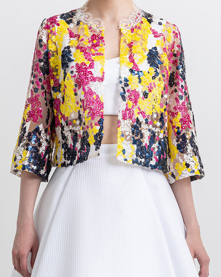 A close-up of an occasion wear featuring a white cropped top paired with a multicolor sequined jacket and a flared white skirt.