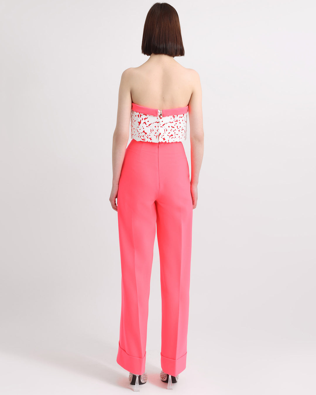 The back of an occasion wear featuring a strapless neon pink top with white laser-cut silicon details matched with a straight cut pants in neon pink.