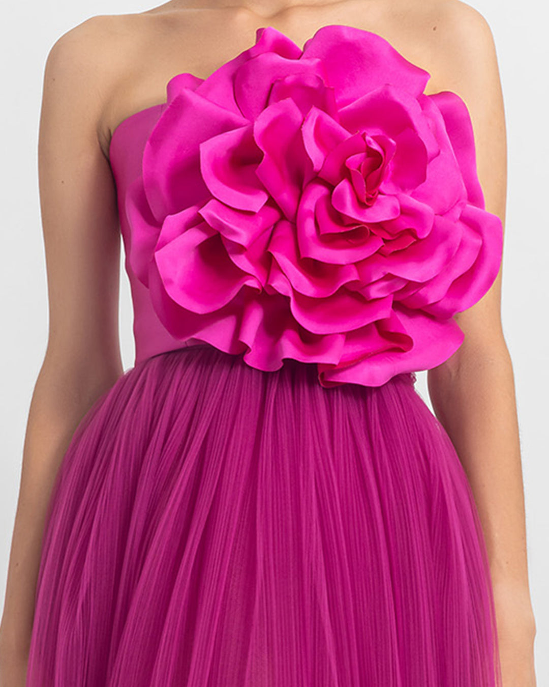 A close-up of a strapless long fuchsia dress with satin flower design on the top and fully-pleated tulle from the bottom.