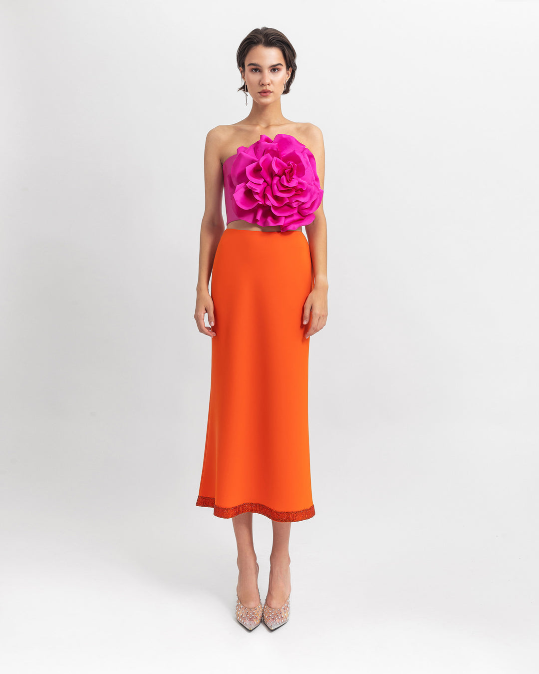 An evening wear set featuring a cropped fucshia flower top paired with a straight cut crepe orange skirt with sequin details on the hemline.