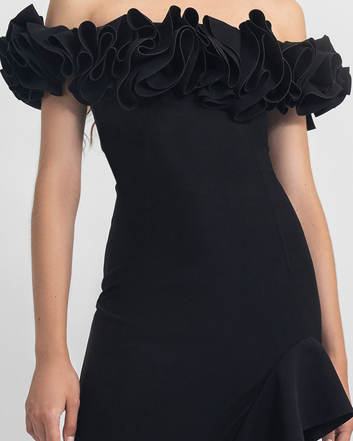 A close-up of a ruffled off-shoulders crepe black dress with an asymmetrical skirt with ruffled details and a slit on the side.