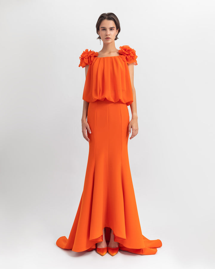 An evening wear set featuring an orange draped loose cut chiffon top with flower details on the shoulders paired with a mermaid cut crepe skirt.