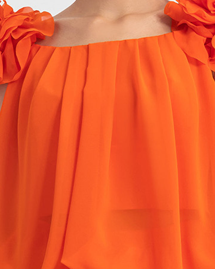 A close-up of an orange draped loose cut chiffon top with flower details on the shoulders.